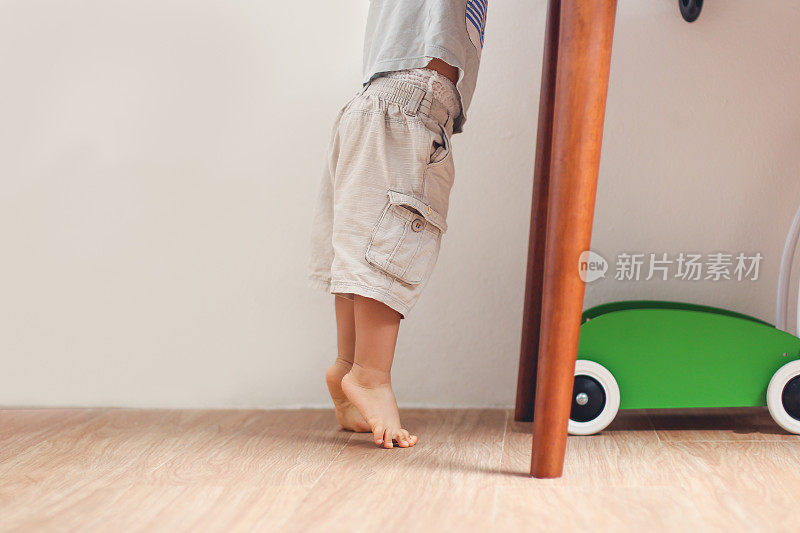 亚洲18个月/ 1岁蹒跚学步的婴儿男孩踮着脚尖站在家里的地板上的特写照片